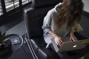 A young woman sits in a leather chair with her laptop working on her self employment adventure. 
