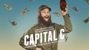 Capital C documentary film poster features a hipster looking man with a long beard holding a bottle in his hand with an open mouthed smile at the camera. The text on the poster reads 'a documentary about the crowd revolution: Capital C. Crowdfunding. Crowdsourcing. Bottle Koozies.