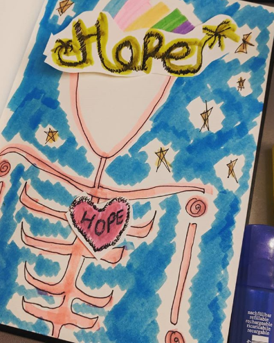 A hand sketched illustration of a skeleton features a sparkler written version of 'hope' on it's triangle head as a crowd and a small heart with hope written on it in the chest. It's a sketch I drew as part of stress reduction during an active leisure session.