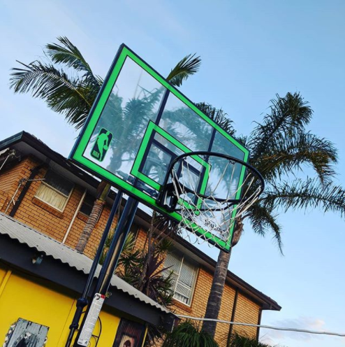 A shot of a basketball hoop is up against a yellow building, framed by palm trees.