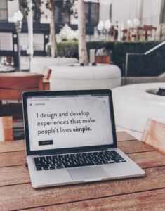 A laptop reads I design and develop experiences that make people's lives simple. It is to demonstrate how rad freelance marketing activities are. It sits on a wooden table in an office.