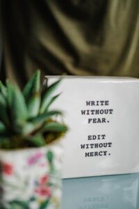 cube reads write without fear. edit without mercy. it sits on a table or bench next to s potted succulent.