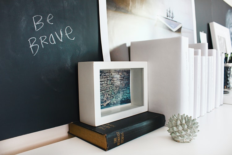 a chalkboard says be brave with a white block in front of it with an old book to signify business bravery