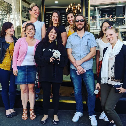 A photo of the Sydney community of freelancers from the Freelance Jungle out front Yullis. There are many women and one man. A short woman in front holds a mascot monkey