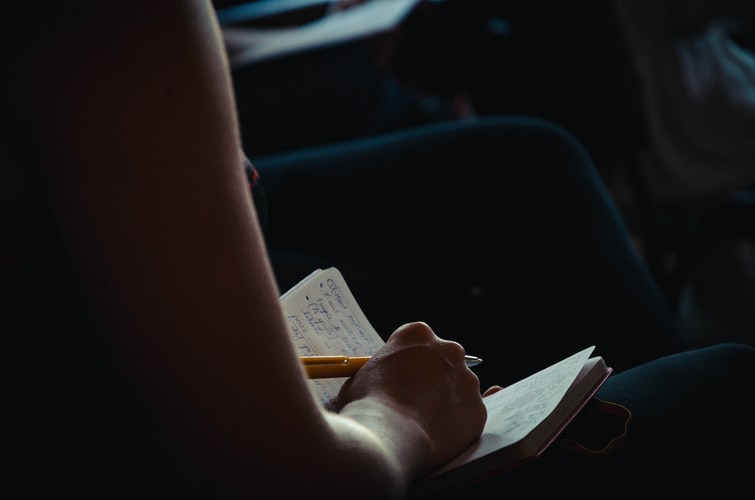 an arm is visible as someone writes their freelance content with pen inside their journal