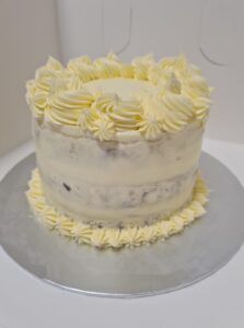 A cream and yellow round cake sits on a silver cardboard platter. It is edged with lemon yellow decorative icing on top and base