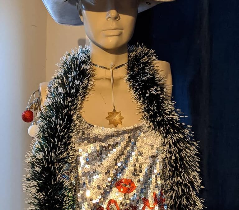 Marlena the mannequin is a size eight in bone white. She's armless because of a few too many drunk people danced with her and broke them. She's got moulded short hair scooped back from her face. She's wearing a silver sequined off the shoulder mini dress that says "kiss me Santa", a silver sequin cowboy hat from Mardi gras' past, a crystal star and a boa made of black and white tinsel.