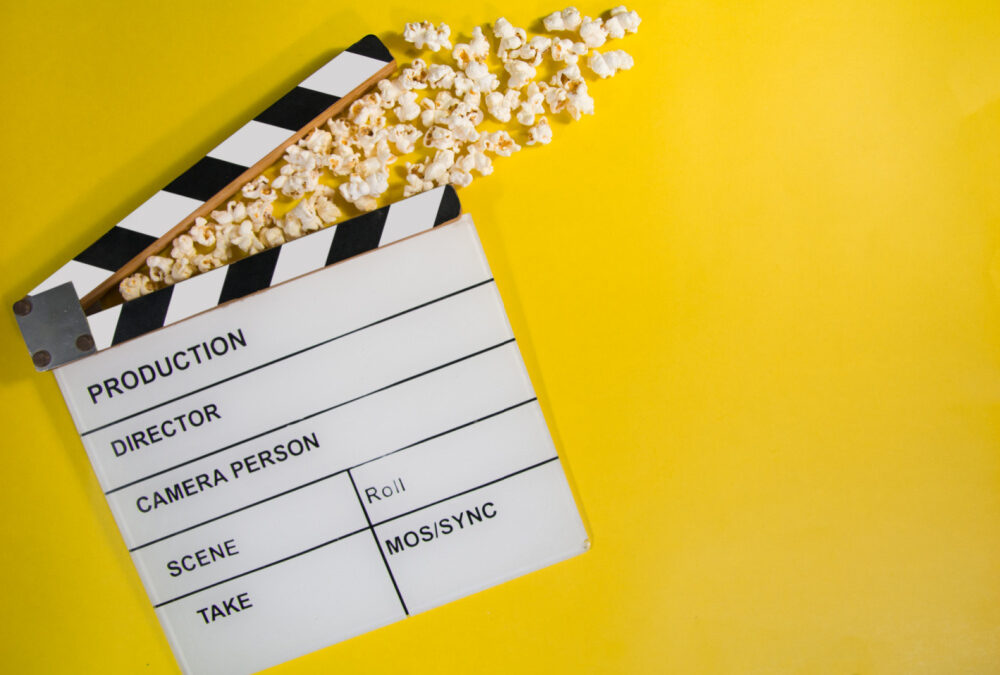 a film clapboard with popcorn is on a yellow background to signify action