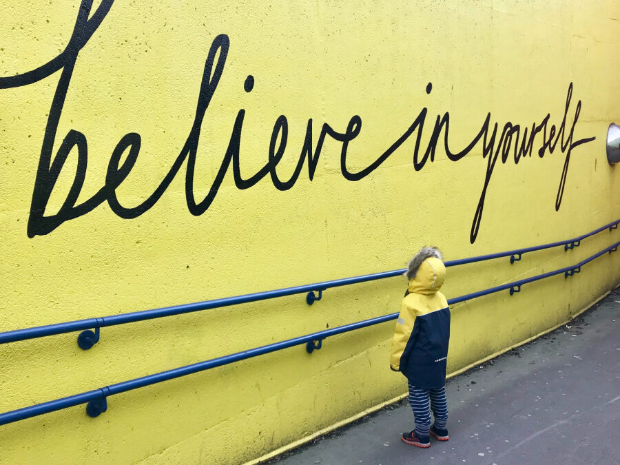a yellow wall reads "believe in yourself" with a kid looking up at it