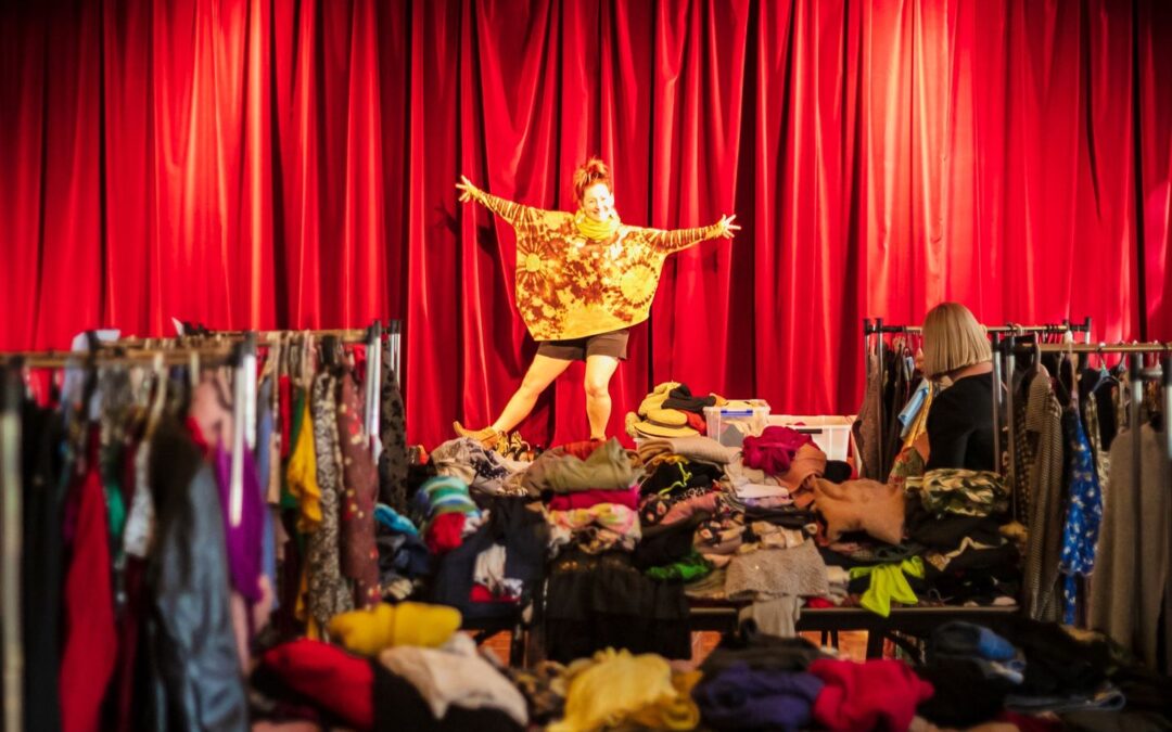 A woman stands on top of a lot of clothing with her arms outstretched