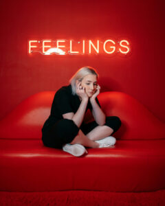 sad woman in a red room with red couch and feelings neon. 