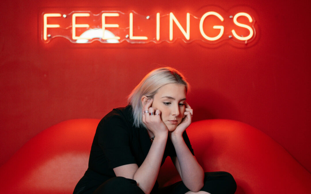 sad looking woman on a couch with neon sign saying feelings to denote a happier creative